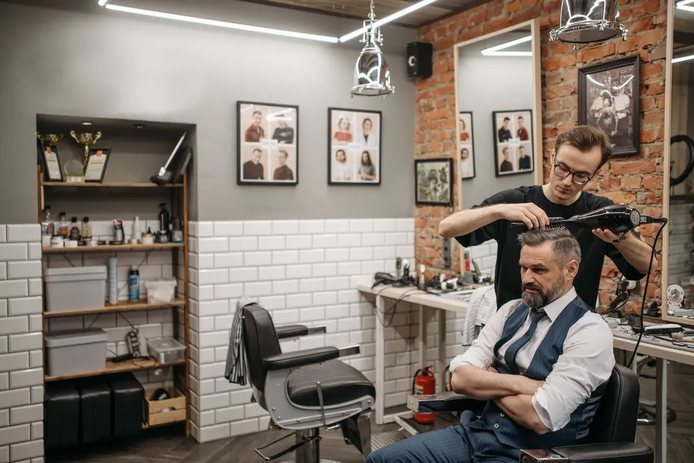 Barbeiro finaliza o corte de um cliente em uma barbearia moderna com parede de tijolos