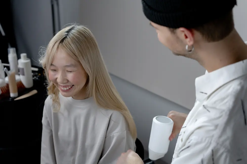 Cabeleireiro finaliza o cabelo de uma cliente sorridente em um salão de beleza