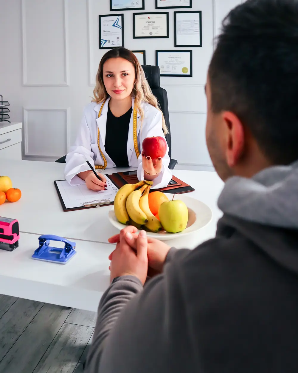 Nutricionista atende um paciente em consultório, com frutas sobre a mesa